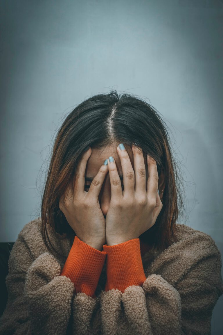A woman in brown sweater covering her face with her hands.